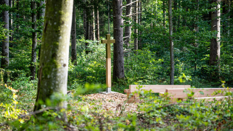 Andachtsplatz der Waldruh Ilkahöhe bei Tutzing am Starnberger See mit Holzkreuz und Sitzbänken inmitten des grünen Waldes.